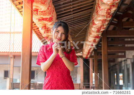 woman wear cheongsam red dress with gesture of congratulation looking at camera in Chinese New Year woman wear cheongsam red dress with gesture of congratulation looking at camera in Chinese New Year 71660281