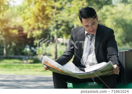 Businessman reading newspaper and looking for new job in public park with copy space. 71661024