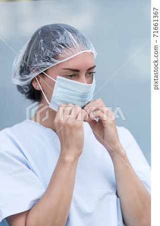 Portrait of a woman doctor putting on and fixing her surgical protective mask before her work shift 71661367