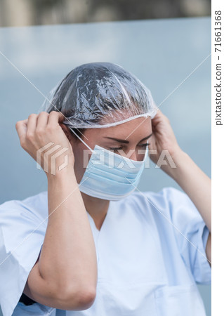 Portrait of a woman doctor putting on and fixing her surgical protective mask before her work shift Portrait of a woman doctor putting on and fixing her surgical protective mask before her work shift 71661368