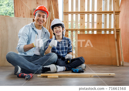 Happy Asian father and son in safety helmet sitting in carpentry workshop at home. Concept family doing hobby together at home. Happy Asian father and son in safety helmet sitting in carpentry workshop at home. Concept family doing hobby together at home. 71661568