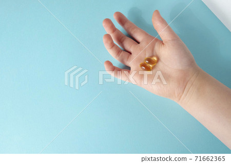 Pile of capsules Omega 3 in hand on blue background. Close up, top view. 71662365