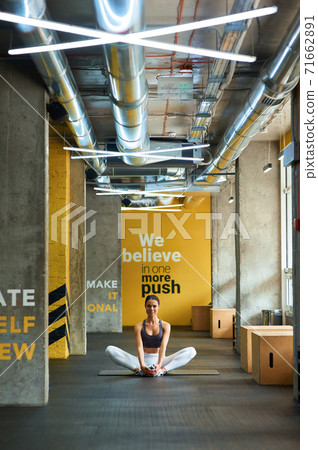 Stretching exercises. Vertical shot of a young fitness woman in sportswear sitting on yoga mat at gym and warming up before workout 71662891
