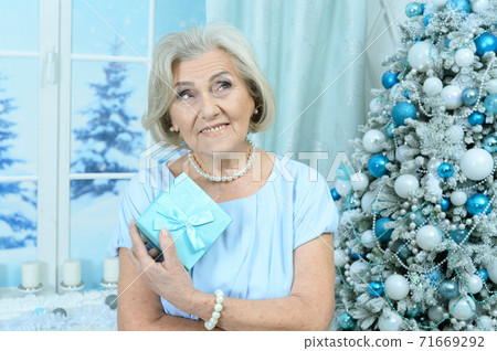 Happy smiling senior woman posing by Christmas tree Happy smiling senior woman posing by Christmas tree 71669292