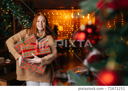 Charming smiling red-haired young woman holding many beautiful Christmas gift boxes. Charming smiling red-haired young woman holding many beautiful Christmas gift boxes. 71671251