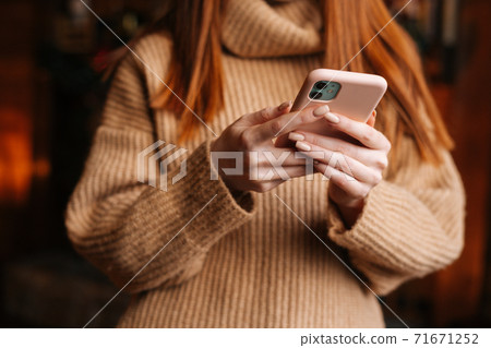 Close-up view of unrecognizable redhead woman wearing winter sweater typing message on mobile phone. Close-up view of unrecognizable redhead woman wearing winter sweater typing message on mobile phone. 71671252