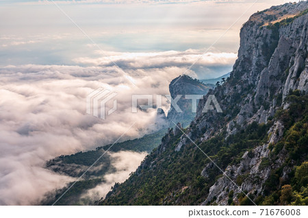 A majestic view of the rocky mountains and the valley in fog and clouds. Creamy fog covered the mountain valley in sunset light. Picturesque and gorgeous scene. Misty sunset over Crimea Mountains 71676008