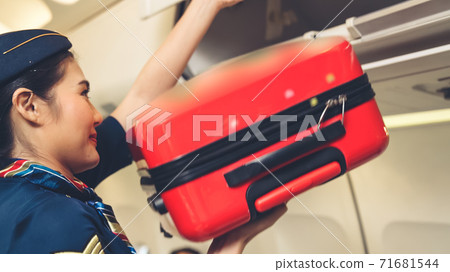 Cabin crew lift luggage bag in airplane 71681544