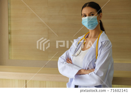 A female doctor wearing a mask is standing at the reception. A female doctor wearing a mask is standing at the reception. 71682141