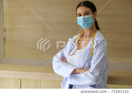 A female doctor wearing a mask is standing at the reception. A female doctor wearing a mask is standing at the reception. 71682142