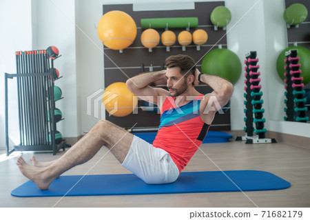Bearded young male doing sit-ups on the blue mat Bearded young male doing sit-ups on the blue mat 71682179