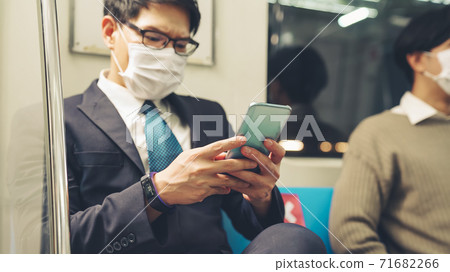 Traveler wearing face mask while using mobile phone on public train 71682266