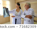 Two doctors are looking at the patient's history and X-Ray film and discussing the patient's illness. 71682309