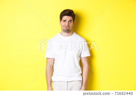Disappointed guy looking upset, sulking and frowning, standing displeased against yellow background 71682440