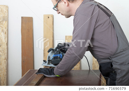Carpenter cuts wood lath electric hand tool circular saw on desk, on background oriented strand board 71690379