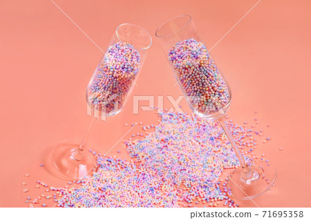 Champagne glasses filled with colorful sugar balls on orange background. Glasses filled with rainbow colored candies, sweet holidays concept. Celebration minimal Christmas party. Champagne glasses filled with colorful sugar balls on orange background. Glasses filled with rainbow colored candies, sweet holidays concept. Celebration minimal Christmas party. 71695358