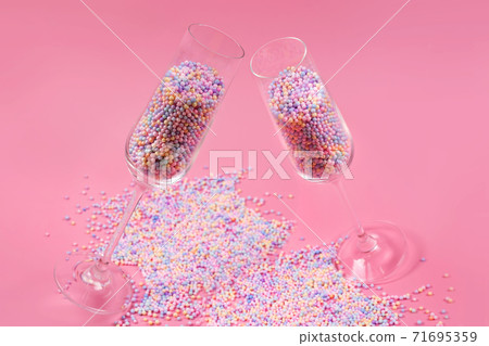 Champagne glasses filled with colorful sugar balls on pink background. Glasses filled with rainbow colored candies, sweet holidays concept. Celebration minimal Christmas party. 71695359