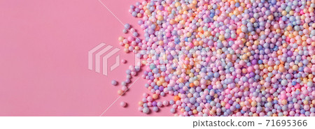 Pile of pastel color balls on pink. Styrofoam or Polystyrene foam background. Mix of colorful sugar balls, used to decorate baking and sweets. Rainbow colored sugar chips, dragee spins, confectionery 71695366