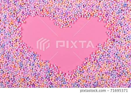 Heart frame made of pastel color balls on pink. Styrofoam or Polystyrene foam background. Mixed colorful sugar balls for sweets decoration. Rainbow sugar candies, dragee, confectionery. Love concept 71695371