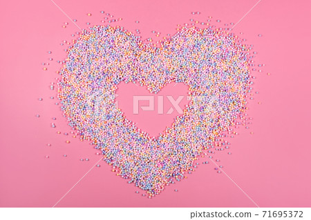 Heart frame made of pastel color balls on pink. Styrofoam or Polystyrene foam background. Mixed colorful sugar balls for sweets decoration. Rainbow sugar candies, dragee, confectionery. Love concept Heart frame made of pastel color balls on pink. Styrofoam or Polystyrene foam background. Mixed colorful sugar balls for sweets decoration. Rainbow sugar candies, dragee, confectionery. Love concept 71695372