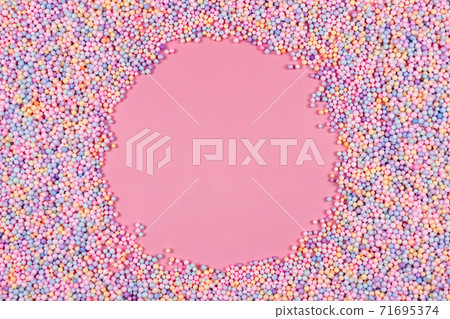 Round frame made of pastel color balls on pink. Styrofoam or Polystyrene foam background. Mix of colorful sugar balls for sweets decoration. Rainbow colored sugar chips, dragee spins, confectionery. 71695374