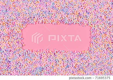 Frame made of pastel color balls on pink. Styrofoam or Polystyrene foam background. Mix of colorful sugar balls for sweets decoration. Rainbow colored sugar chips, dragee spins, confectionery. 71695375