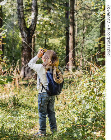 Curious boy is hiking in forest. Outdoor leisure activity for kids. Child looks through binoculars on tree foliage. Sunny day at autumn or summer day. Curious boy is hiking in forest. Outdoor leisure activity for kids. Child looks through binoculars on tree foliage. Sunny day at autumn or summer day. 71696457