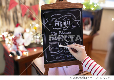 Woman drawing christmas menu of cocoa bar on small chalkboard. Woman drawing christmas menu of cocoa bar on small chalkboard. 71697750