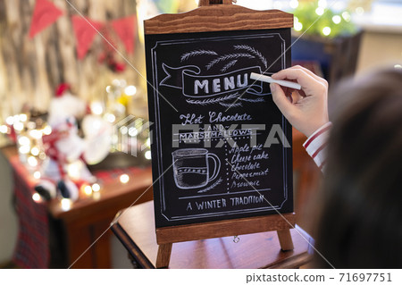 Woman drawing christmas menu of cocoa bar on small chalkboard. Woman drawing christmas menu of cocoa bar on small chalkboard. 71697751
