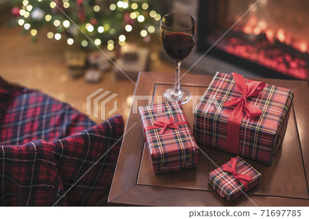 Armchair with plaid, packing gift boxes for family and glass of wine near christmas tree and fireplace. Top view 71697785