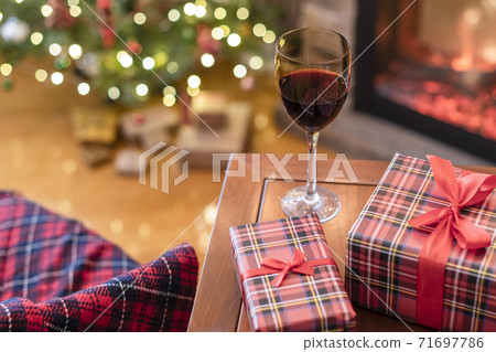 Armchair with plaid, packing gift boxes for family and glass of wine near christmas tree and fireplace. Top view Armchair with plaid, packing gift boxes for family and glass of wine near christmas tree and fireplace. Top view 71697786