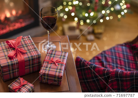 Armchair with plaid, packing gift boxes for family and glass of wine near christmas tree and fireplace. Top view Armchair with plaid, packing gift boxes for family and glass of wine near christmas tree and fireplace. Top view 71697787