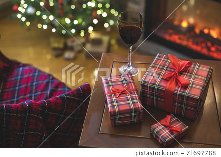 Armchair with plaid, packing gift boxes for family and glass of wine near christmas tree and fireplace. Top view Armchair with plaid, packing gift boxes for family and glass of wine near christmas tree and fireplace. Top view 71697788
