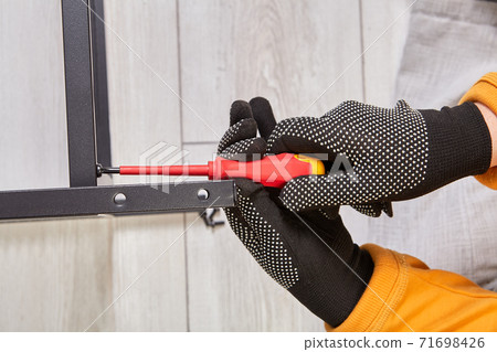 A worker assembles a metal frame for furniture using screwdriver. 71698426