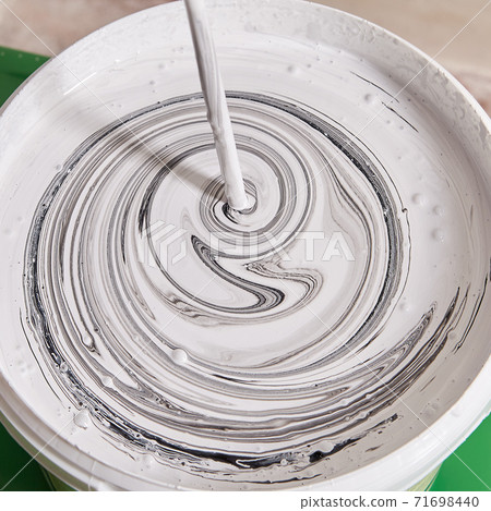 Handyman is mixing paints in basket using drill to paint walls. 71698440