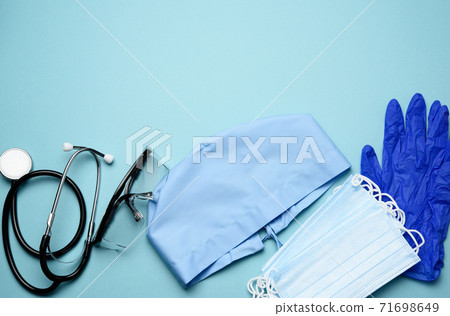 textile blue cap, disposable medical mask, pair of gloves and plastic glasses on a blue background 71698649