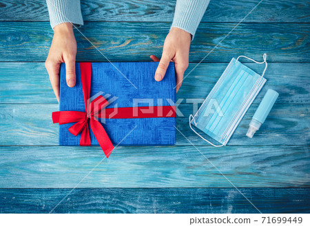 Woman's hands holding present box. Conceptual symbol of the Christmas in pandemia of COVID19. 71699449