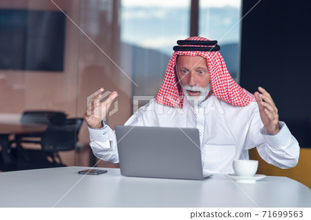 Arab businessman looks surprised while using a laptop Arab businessman looks surprised while using a laptop 71699563