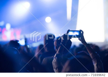 Silhouette of raised hands holding a smart phone recording music concert 71699642