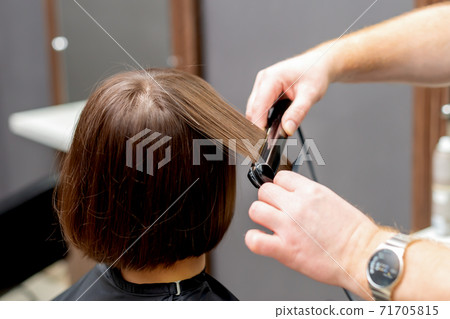 Hairdresser straightens hair of woman. 71705815
