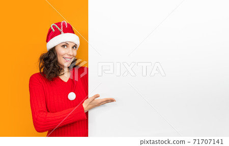 Young girl in santa claus hat on bright color background make gesture hand. New Year and Christmas celebration concept. Woman in red hat stands having smiling showing with hand on copy space 71707141
