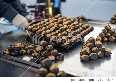 Male salesman is cooking Roasted chestnuts on a city street. Street food, hot cooked chestnuts Male salesman is cooking Roasted chestnuts on a city street. Street food, hot cooked chestnuts 71708182