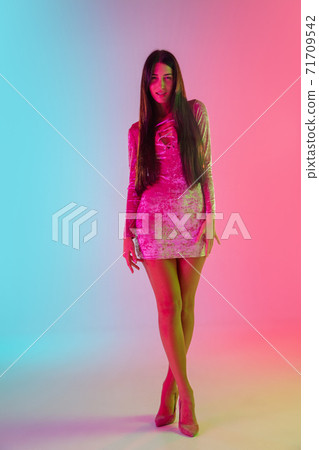 Beautiful seductive girl in fashionable dress, outfit on bright gradient pink-blue background in neon light 71709542