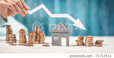 Woman holds an arrow down over model of the house and stack of coins. 71712612