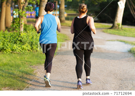 Two women on a dirt path running around a lake in the woods Two women on a dirt path running around a lake in the woods 71712694