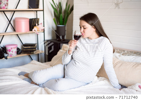 Pregnant woman keeping glass of wine. Future mother drinking alcohol while expecting little baby 71712740