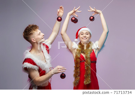 guy and girl in Santa costumes at a photo shoot in the Studio. guy puts Christmas decorations on a girl guy and girl in Santa costumes at a photo shoot in the Studio. guy puts Christmas decorations on a girl 71713734