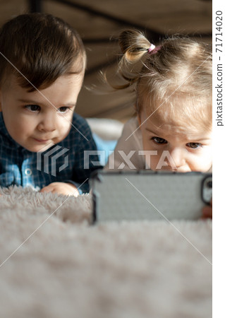 friendship, childhood, technology concepts - 2 young children baby of different nationalities Persian and Slavic appearance watch cartoon on smartphone on bed. kids preschool speak by video conference 71714020