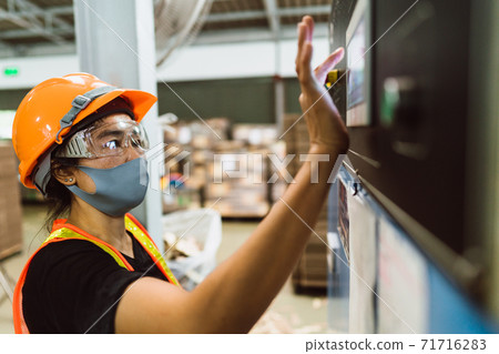 Professional Industrial worker operate screen panel of heavy machine to setting a mechanic controller in factory atmosphere, Technician female engineer with safety wear and face mask in heavy factory. 71716283