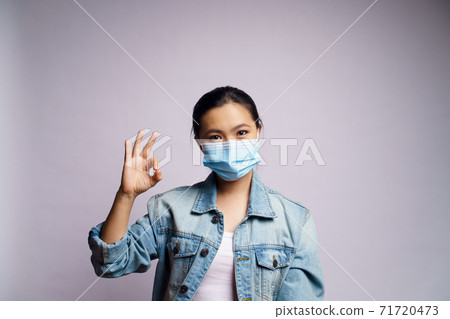 Asian woman wearing protective face mask and showing OK sign isolated over white background. Asian woman wearing protective face mask and showing OK sign isolated over white background. 71720473